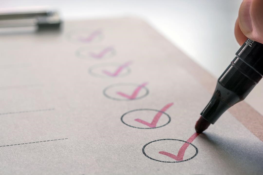 A checklist with multiple items being marked with red check marks by a person using a marker.